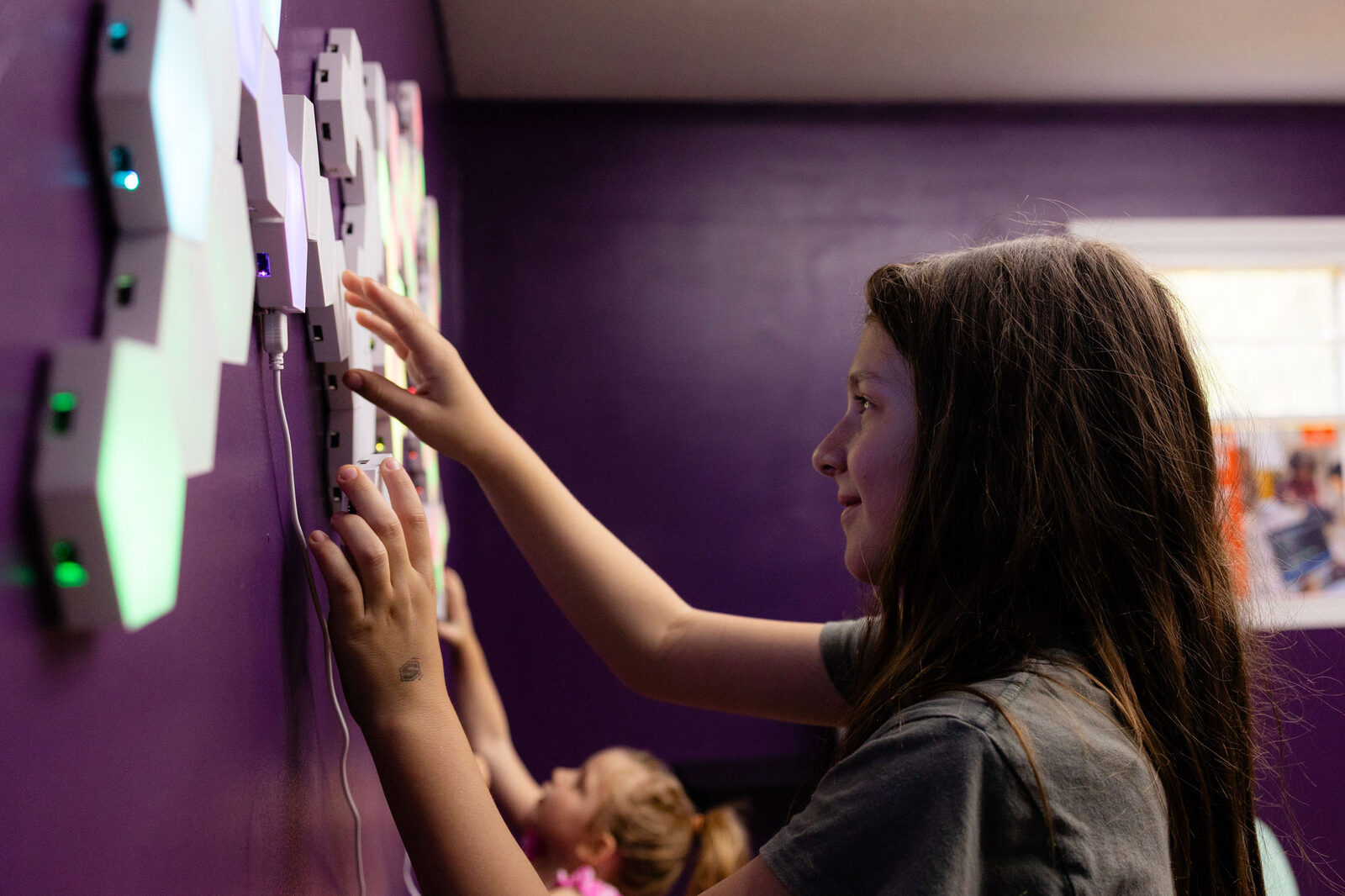 A Talent School learner illuminated by color-shifting neon light panels on a deep purple wall.