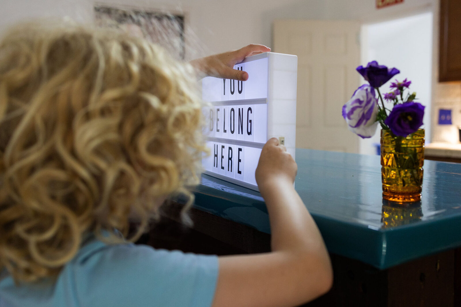 A young learner arranging letters that spell 'You Belong Here' beside a vase of flowers.